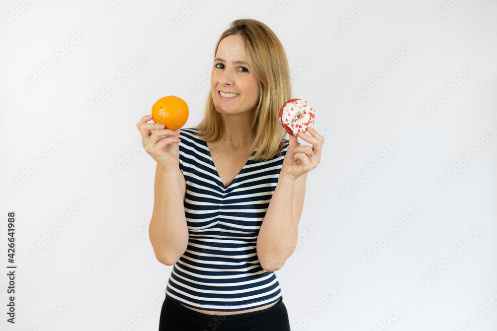 Happy woman holding orange fruit and donuts in hands. Healthy life, diet and nutrition concept. Happy woman holding orange fruit and donuts in hands. Healthy life, diet and nutrition concept.