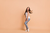 Full size profile photo of optimistic brunette girl dance sing wear white top jeans sneakers isolated on beige background