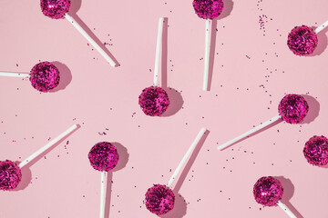 Creative pattern with lollipops and bright pink glitter on pastel pink background. Party fun happy life concept. Minimal flat lay with candy.