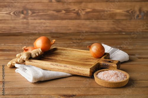 Cutting board with onions and ginger on wooden background