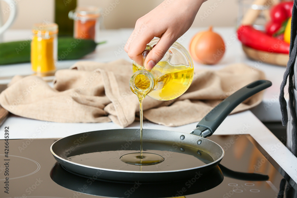 Woman pouring oil onto frying pan in kitchen