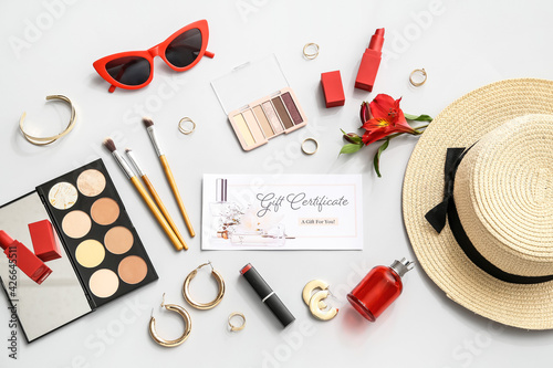 Gift certificate, decorative cosmetics and female accessories on light background