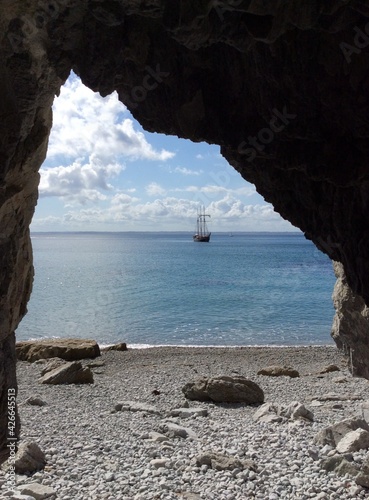 View from a cave to the bay with sailing boat in the distance