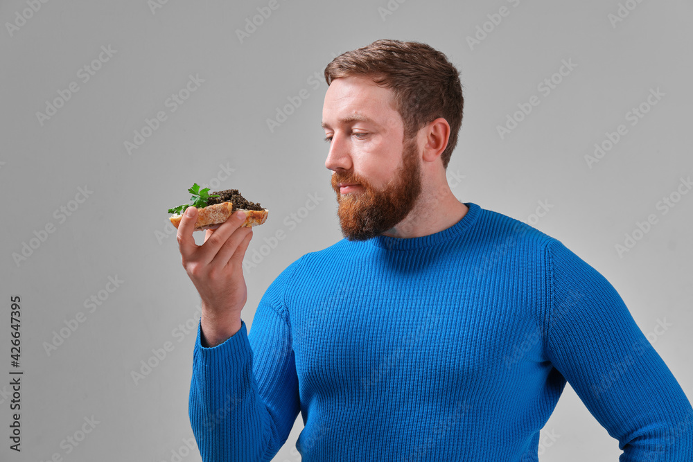 young man with a sandwich with wild black beluga caviar on a light uniform background young man with a sandwich with wild black beluga caviar on a light uniform background