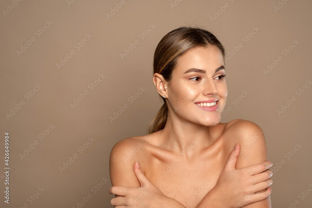 Obraz premium Young lovely woman is touching her shoulder. Beautiful face of young woman with clean fresh skin close up on beige background. Skin care face . Cosmetology