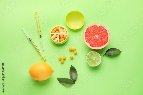 Fototapeta Naklejka Na Ścianę i Meble -  Syringes with vitamin C, pills and citrus fruits on color background