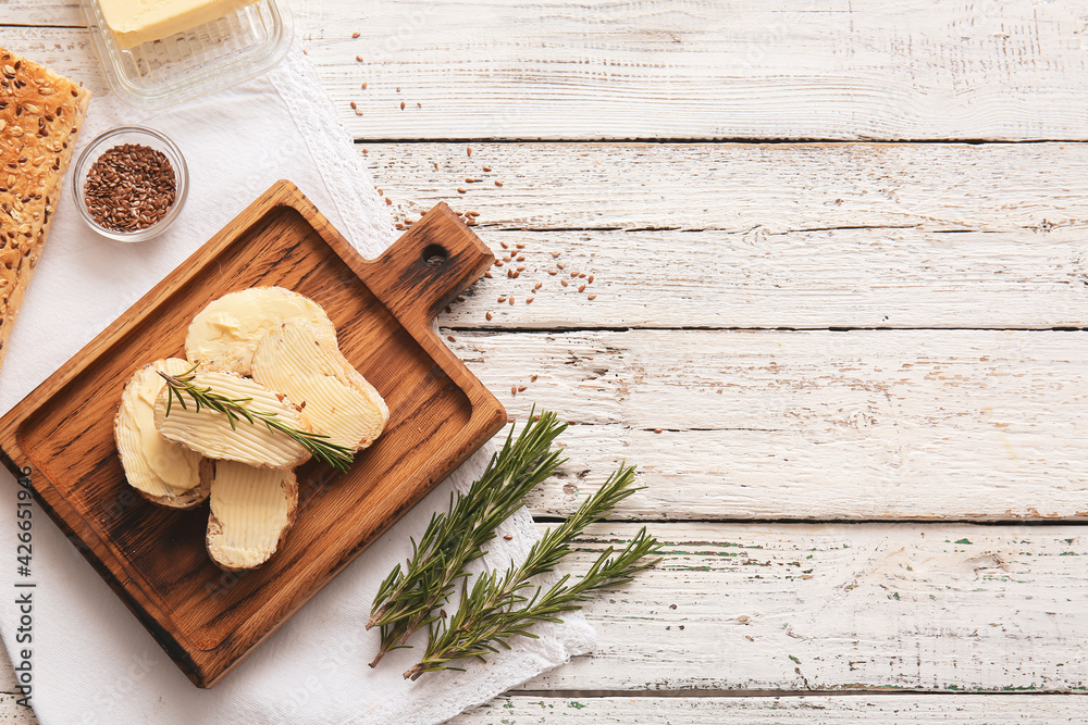 Fototapeta premium Slices of fresh bread with butter, flax seeds and rosemary on light wooden background