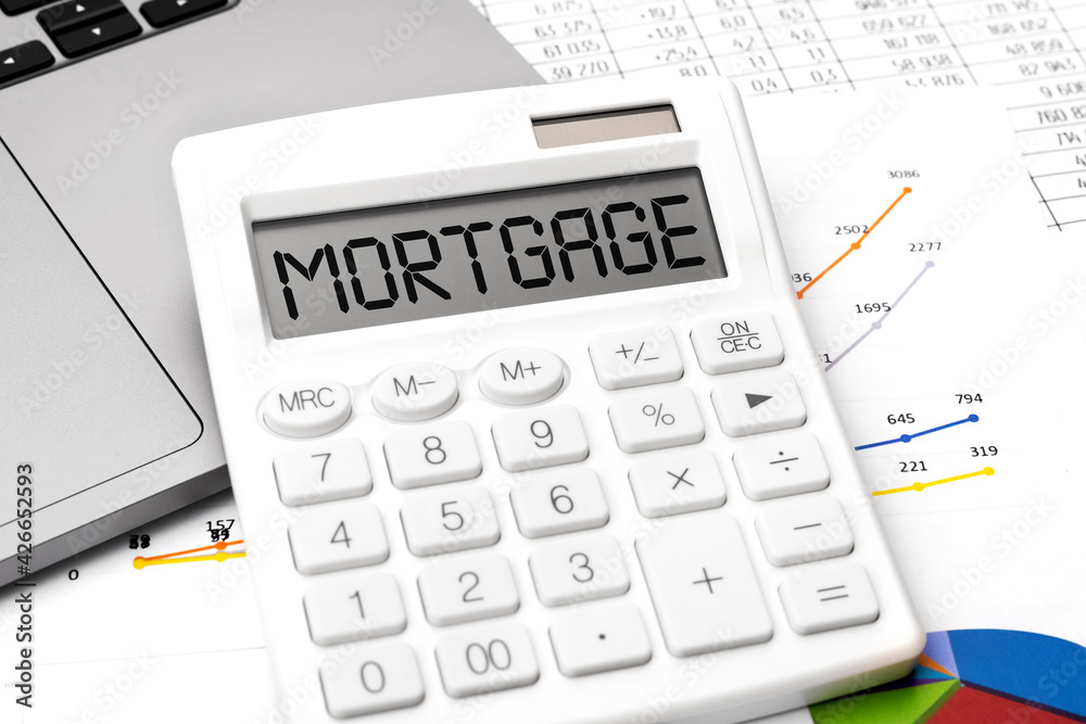 Word MORTGAGE on calculator on laptop with paper with charts. Top view. Word MORTGAGE on calculator on laptop with paper with charts. Top view.