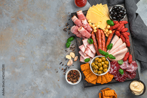 Meat delicacies, cheese, olives, sauces and crackers on a gray background with space to copy.