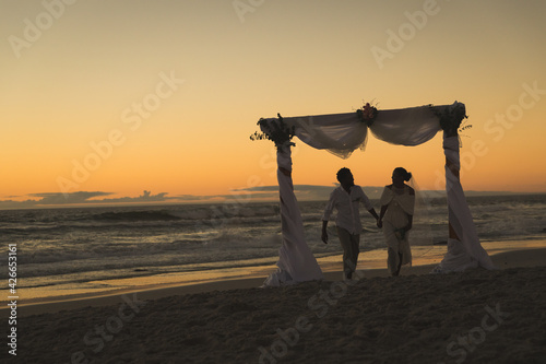 African american couple in love getting married, walking on beach during sunset holding hands