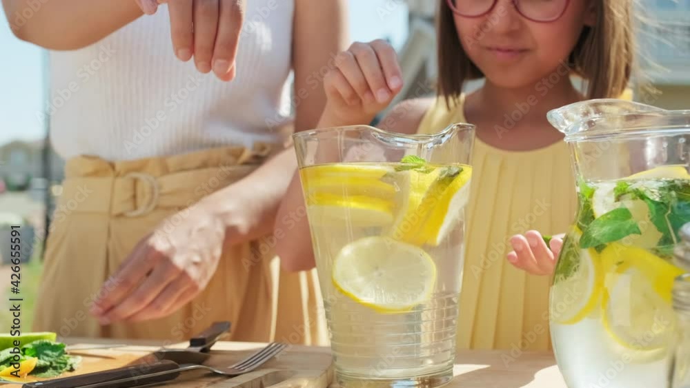 Midsection shot of cute 10-year-old girl adding some mint leaves to lemonade then stirring it in glass decanter standing outdoors on sunny summer day Midsection shot of cute 10-year-old girl adding some mint leaves to lemonade then stirring it in glass decanter standing outdoors on sunny summer day