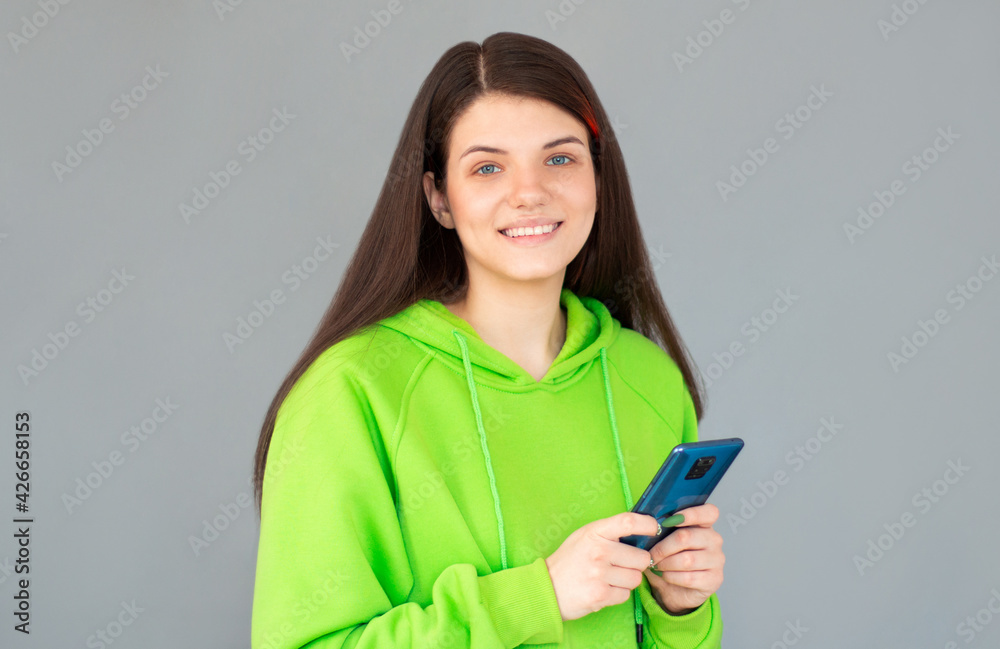 Smiling woman with smartphone in hands looking at the camera over gray background Smiling woman with smartphone in hands looking at the camera over gray background