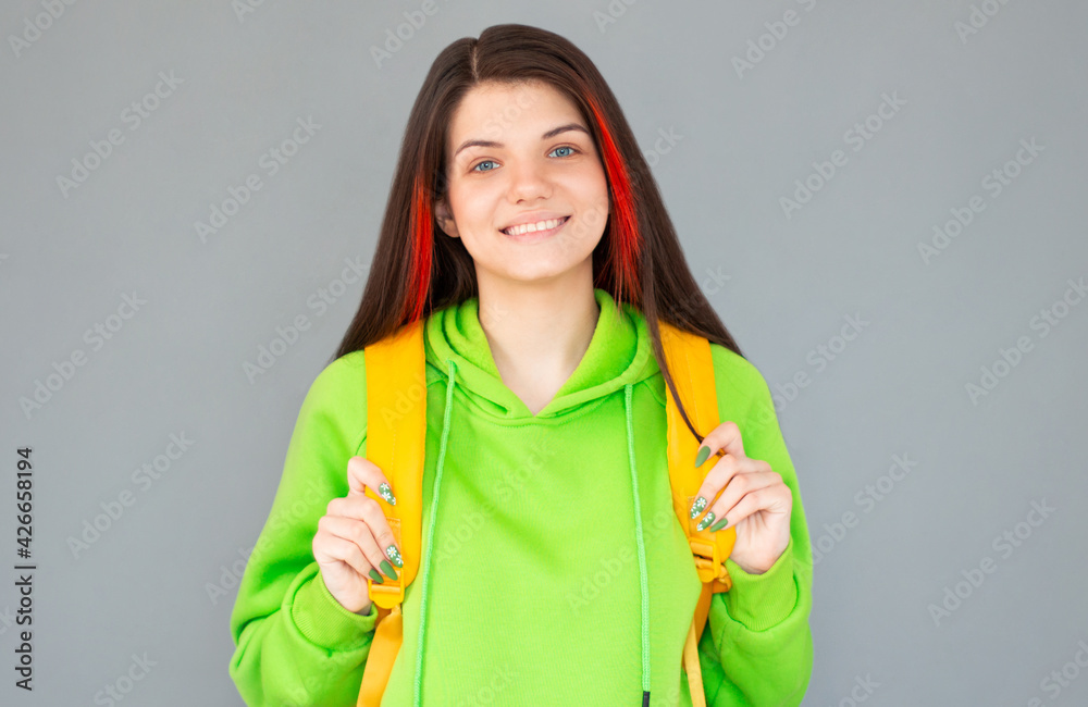 Indoor picture of young good-looking teenage girl isolated on gray background with yellow backpack Indoor picture of young good-looking teenage girl isolated on gray background with yellow backpack