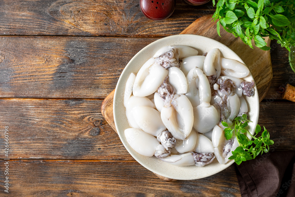 Raw cuttlefish in a ceramic plate on the kitchen table. Lots of peeled squid in a bowl on a brown wooden table top view. The concept of cooking shellfish