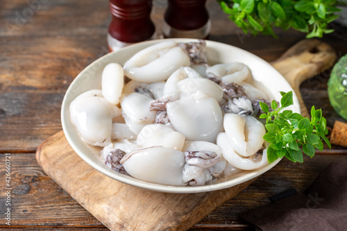 Obraz na płótnie Raw cuttlefish in a ceramic plate on the kitchen table. Lots of peeled squid in a bowl on a brown wooden table. The concept of cooking shellfish w salonie