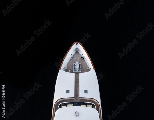 High angle aerial bird's eye partial view of the bow of a long white luxury yacht with wooden deck in dark blue waters shortly after sunset in Sydney, Australia with a lot of copy space.
