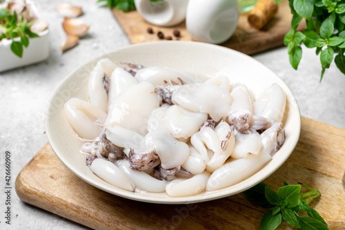 Raw cuttlefish in a ceramic plate on the kitchen table. Lots of peeled squid in a bowl on a light background. The concept of cooking shellfish
