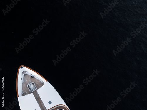 High angle aerial bird's eye partial view of the bow of a long white luxury yacht with wooden deck in dark blue waters shortly after sunset in Sydney, Australia with a lot of copy space. © Juergen Wallstabe