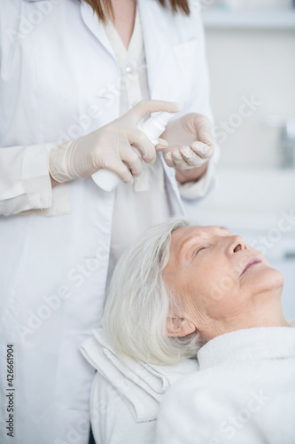 Cosmetologist working with a mature customer and preparing face cream for applying