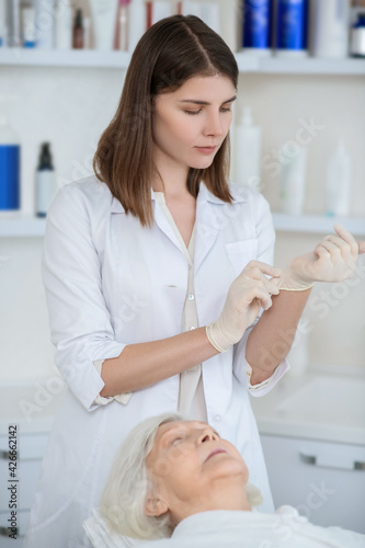 Cosmetologist in a white coat putting on sterile gloves
