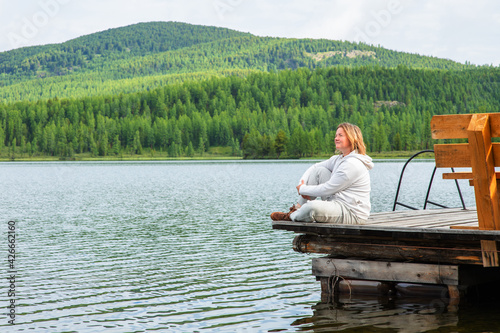 A woman sits on the pier of a blue lake in the mountains and looks into the distance © Ermolaeva Olga