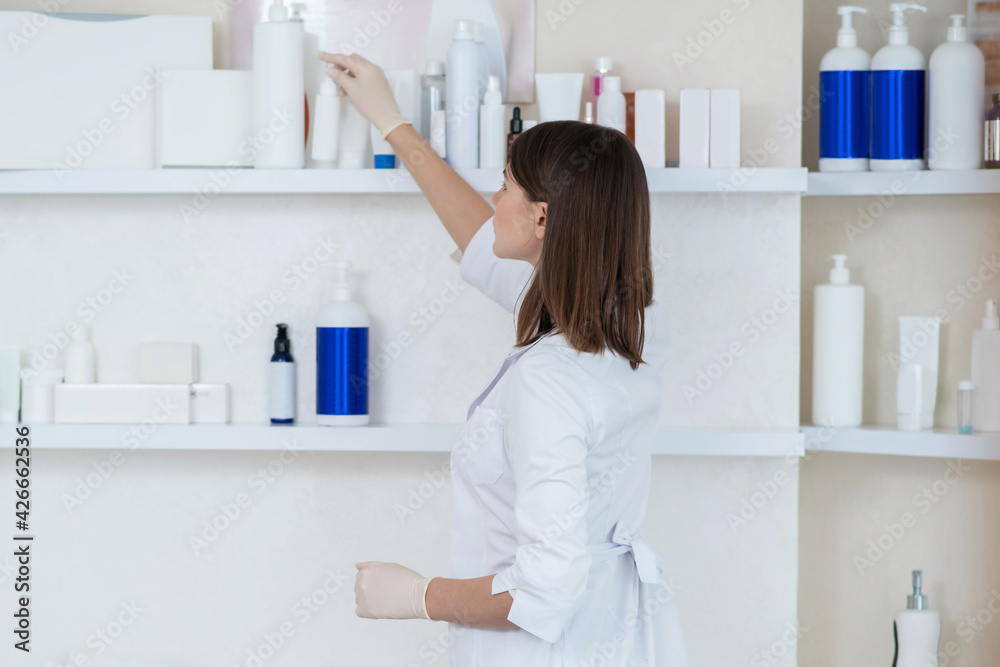 Cosmetologist in a white coat taking beauty products from the shelf