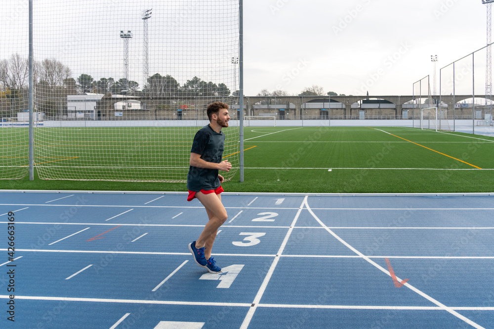 Fototapeta premium Hard working young runner boy doing warm-up in blue running track.