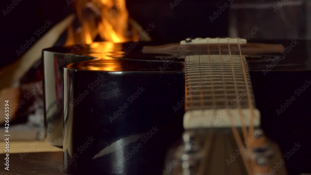 Change of focus on the strings of an acoustic guitar in the flickering light against the background of the flame. Close-up. Change of focus on the strings of an acoustic guitar in the flickering light against the background of the flame. Close-up.