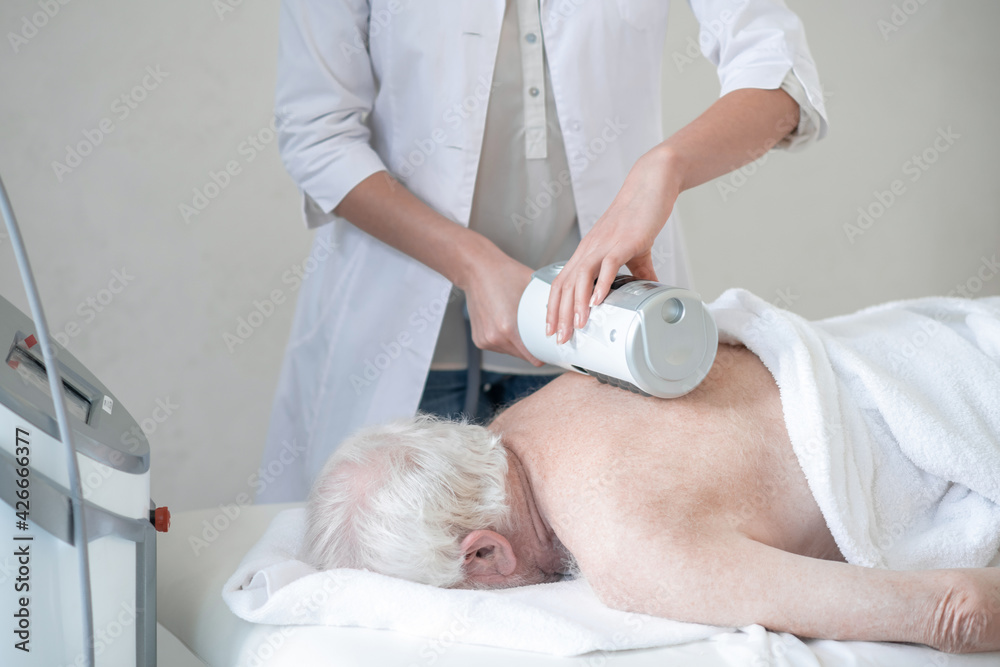 Massage therapist doing back massage procedures to a gray-haired woman Massage therapist doing back massage procedures to a gray-haired woman