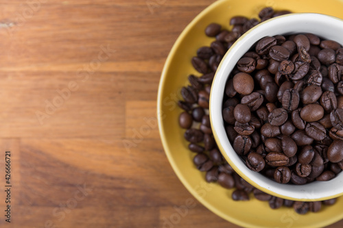 coffee cup top view, yellow ceramic cup and saucer filled with coffee beans on a wooden surface, with space to write to the left, horizontal photo