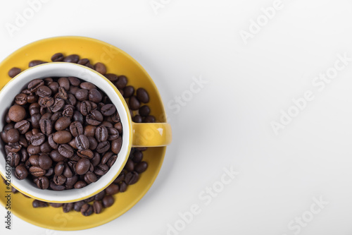 coffee cup top view, yellow ceramic half cup filled with coffee beans on a white surface with space for writing on the right, horizontal photo