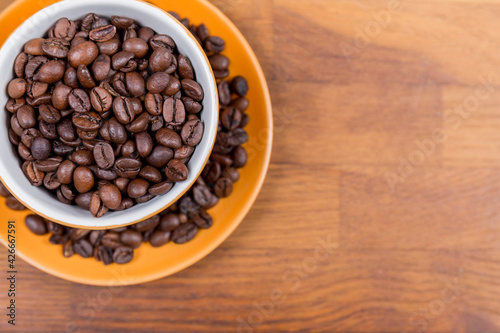 coffee cup top view, orange ceramic cup and saucer filled with coffee beans on a wooden surface, with space to write to the right, horizontal photo