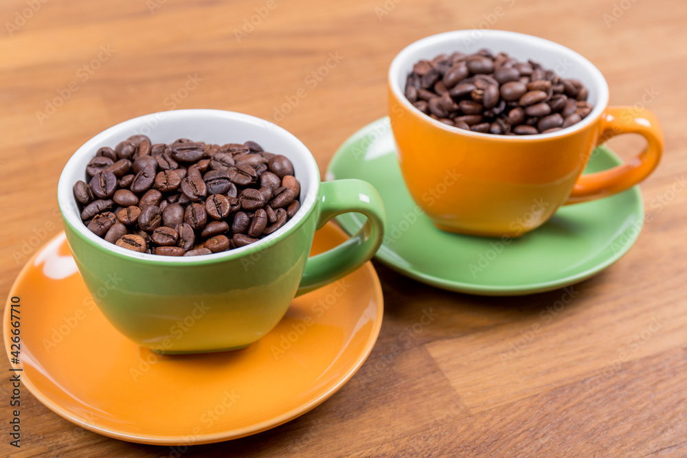 coffee composition, close-up of two cups of coffee one orange and one green with their plates full of coffee beans on a wooden surface, horizontal photo coffee composition, close-up of two cups of coffee one orange and one green with their plates full of coffee beans on a wooden surface, horizontal photo