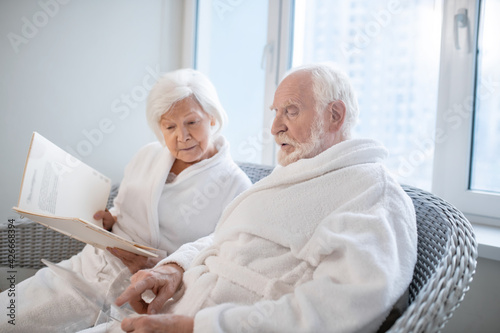 Senior couple in white robes choosing procedures in a spa center