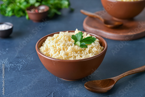 Bowl with tasty couscous and parsley on dark background