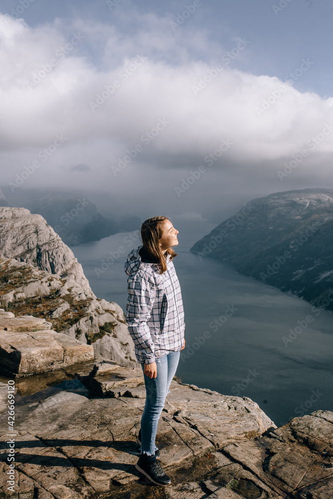 Naklejka premium A pretty girl stands on top of Mount Preikestolen (Pulpit Rock) in Norway
