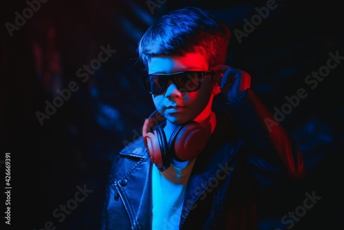 Studio shot in dark studio with neon light. Portrait of a stylish boy with headphones