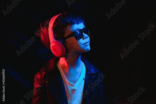 Studio shot in dark studio with neon light. Portrait of a stylish boy with headphones