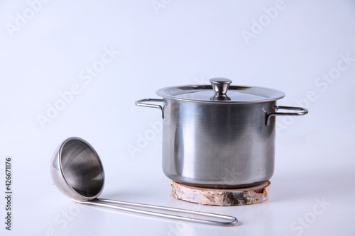 metal saucepan on wooden pedestal and soup ladle isolated on white background