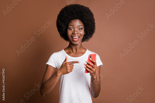 Portrait of astonished attractive dark skin person indicate finger phone isolated on brown color background