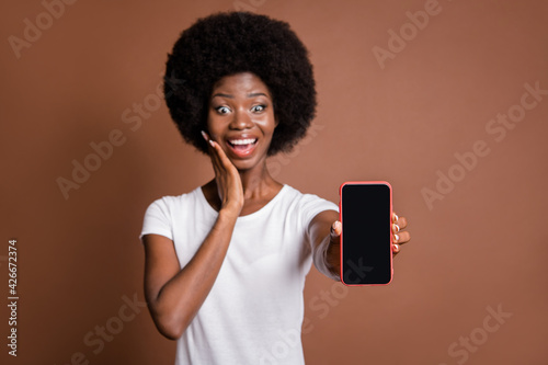 Photo portrait of woman touching cheek amazed showing blank space display of smartphone isolated on brown color background