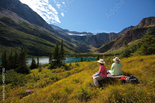 2 people sitting on a bench in beautiful Mountain setting with a lake on a sunny day.