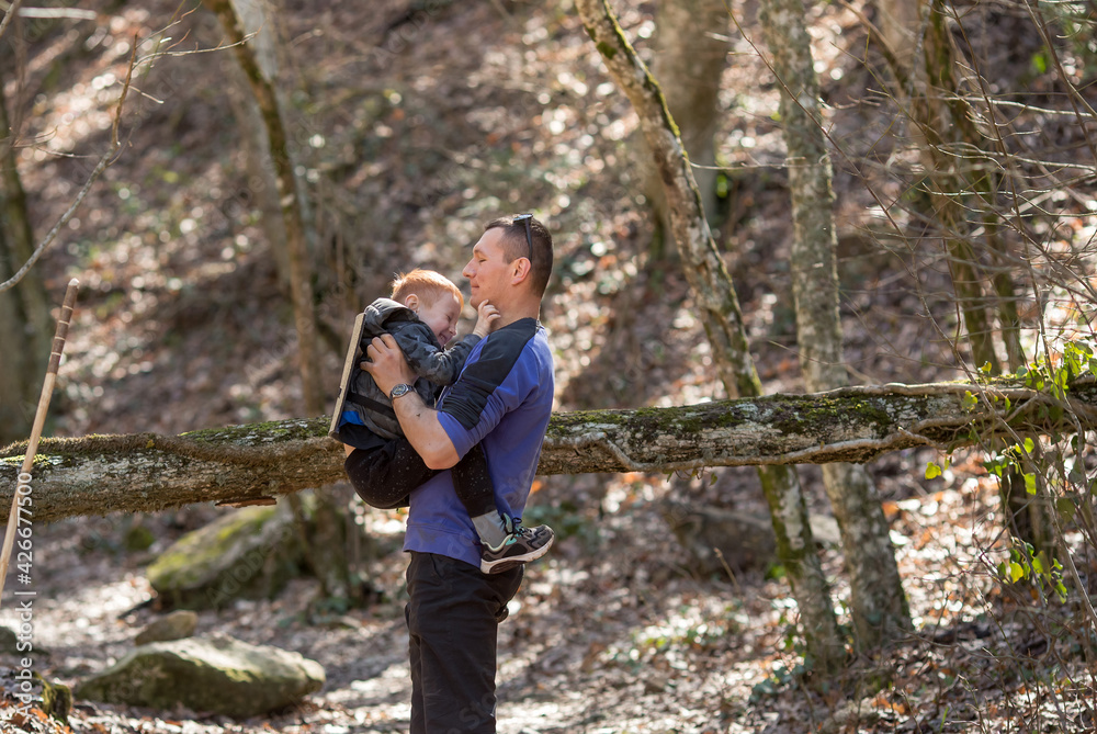 dad holds his son in his arms in the woods to get him hooked on a tree