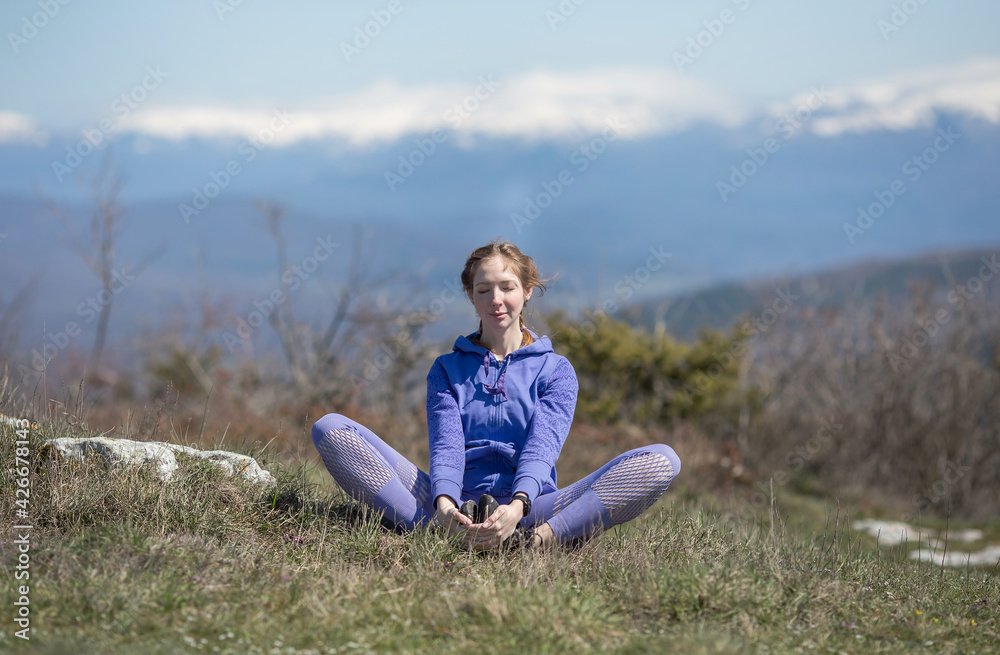 A girl in sports clothes sits on a mountain in the lotus position and meditates, does breathing exercises A girl in sports clothes sits on a mountain in the lotus position and meditates, does breathing exercises