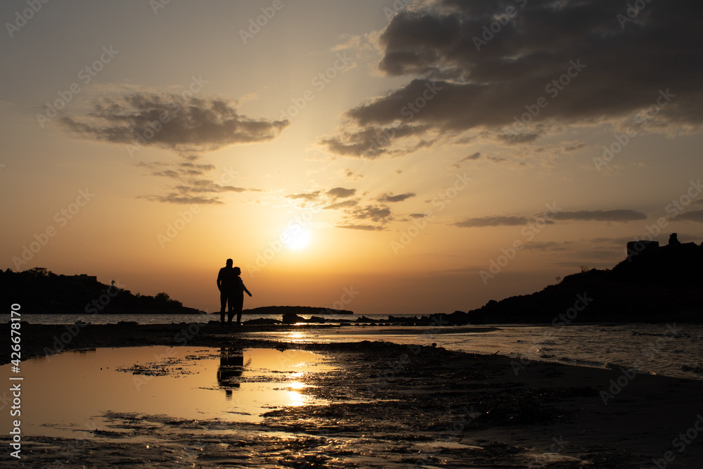 Fototapeta premium People's silhouette walking at the beach with the sunset at background