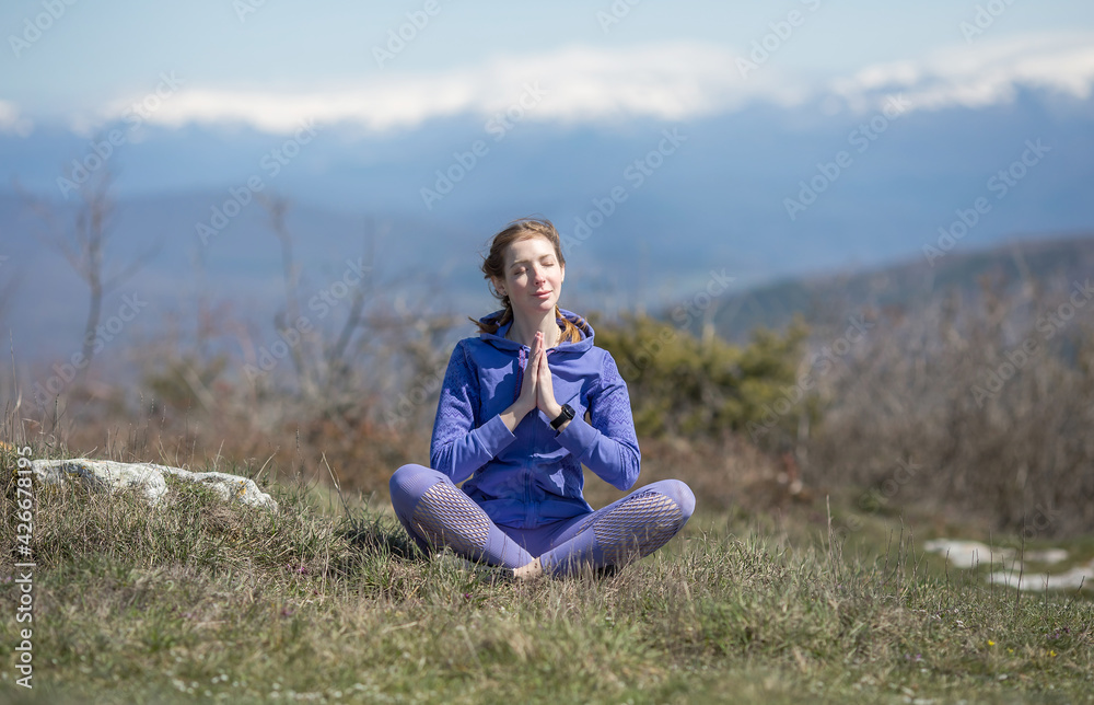 A girl in sports clothes sits on a mountain in the lotus position and meditates, does breathing exercises A girl in sports clothes sits on a mountain in the lotus position and meditates, does breathing exercises