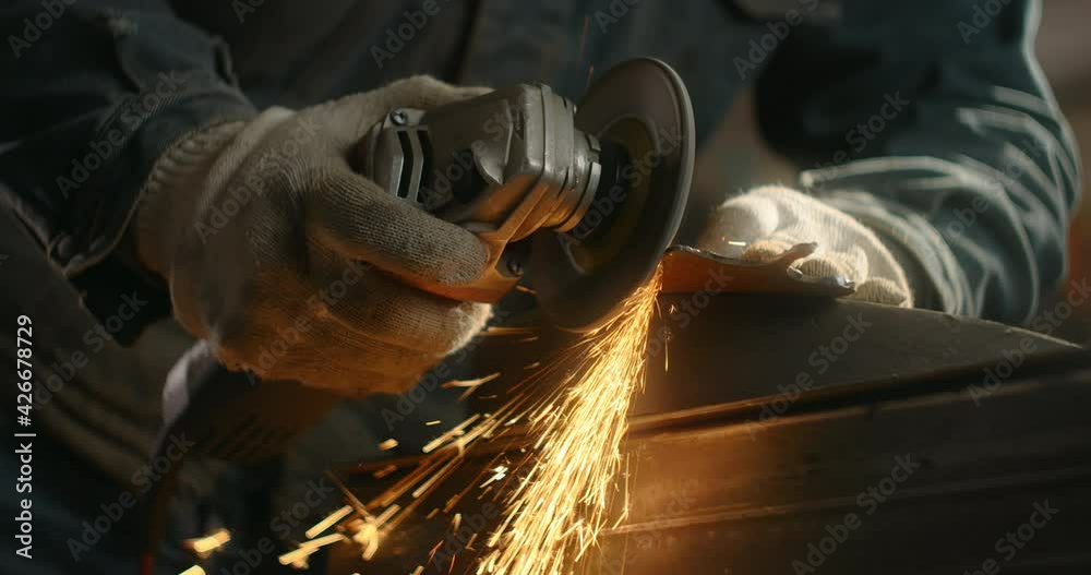 Locksmith sands the edges of a metal detail by electric grinder with a lot of sparks in slow motion, metalwork at workshop, 4k 60p Prores HQ