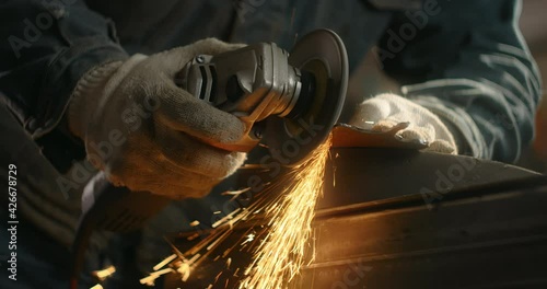 Locksmith sands the edges of a metal detail by electric grinder with a lot of sparks in slow motion, metalwork at workshop, 4k 60p Prores HQ photo