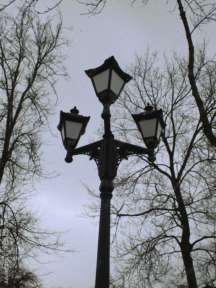 black lamppost with three lanterns against a gray evening spring sky