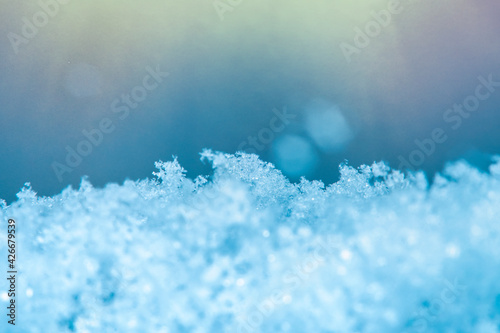 Background with close-up of snow under strong magnification with bright sunlight. Slightly melted snow with sharp edges in soft focus.